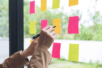 Cropped hand of businesswoman writing on adhesive note