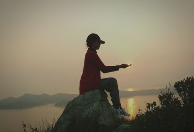 Man sitting on mountain against sky during sunset