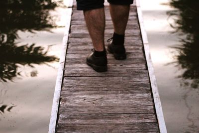 Low section of man standing on boardwalk over lake