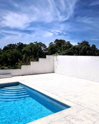 Swimming pool by trees against sky