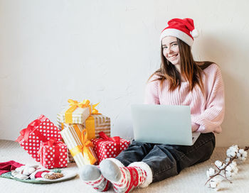 Young woman in santa hat shopping online surrounded by presents