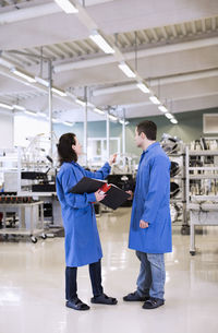 Female electrician pointing while discussing with colleague in factory