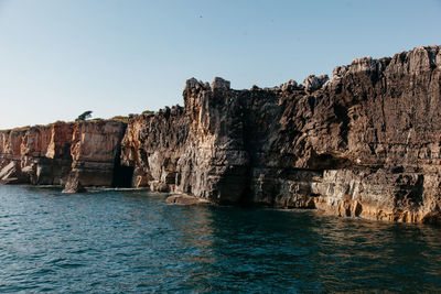 Scenic view of sea by cliff against clear sky