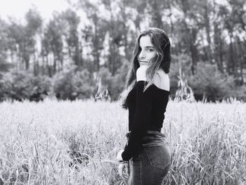 Portrait of young woman standing amidst grassy field