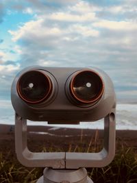 Close-up of coin-operated binoculars by sea against sky