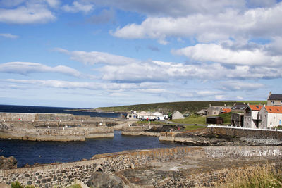 View of houses by calm sea against cloudy sky