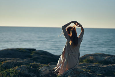 Woman standing on rock by sea against sky