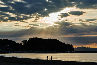 Silhouette people on beach against sky during sunrise