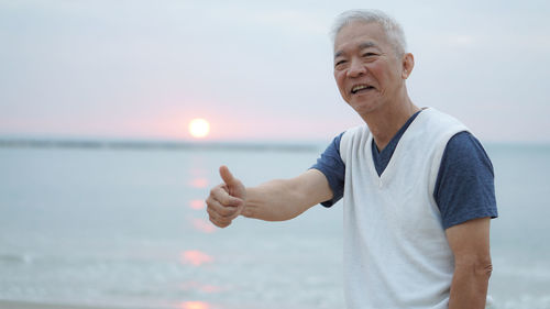 Man gesturing against sea during sunset