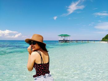 Young woman wearing sunglasses standing at beach against sky