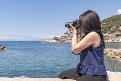 Rear view of woman photographing sea against sky