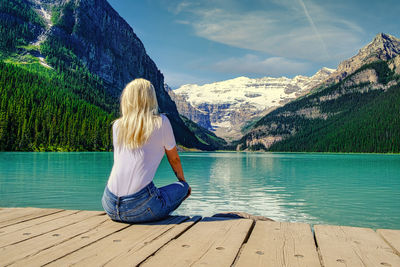 Rear view of woman sitting by lake louise against mountain