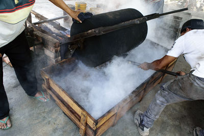 Male workers roasting coffee beans in container on fire pit