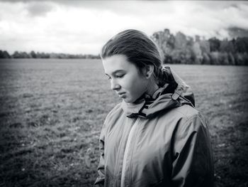 Girl in jacket looking down while standing on field