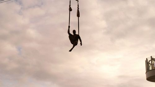 Low angle view of man hanging against sky