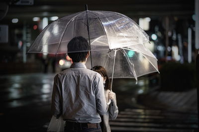 Rear view of man with umbrella standing in rain