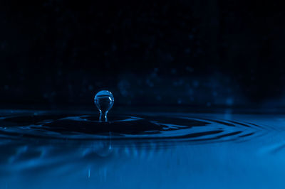 Close-up of droplet falling in water against black background