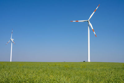 Windmills on field against clear blue sky