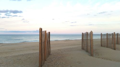 Wooden posts on beach against sky during sunset