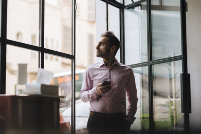 Contemplative businessman with smart phone standing by door