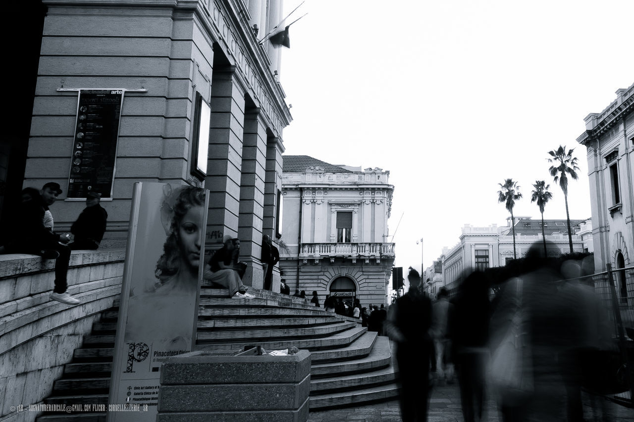 architecture, building exterior, built structure, walking, city, building, men, street, clear sky, city life, person, lifestyles, full length, street light, city street, day, incidental people, residential building, the way forward