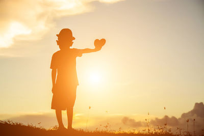 Silhouette man standing on field against sky during sunset