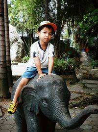 Portrait of boy sitting by tree against plants