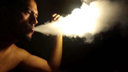 Shirtless man exhaling smoke in darkroom