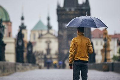 Rear view of man walking on street during rainy season