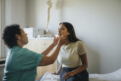 Female physician checking throat of young woman sitting in clinic