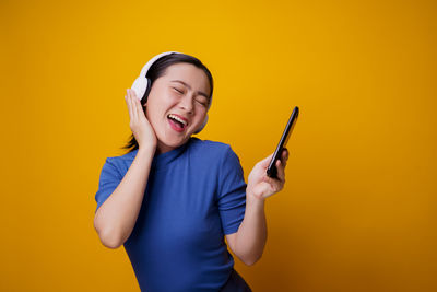 Young man using mobile phone against yellow background