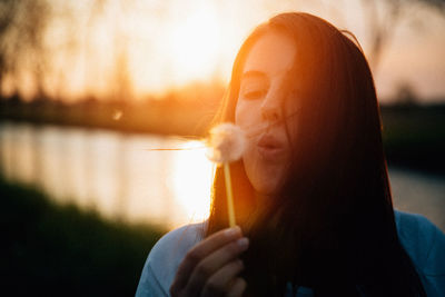 Close-up of woman holding drink against sky at sunset