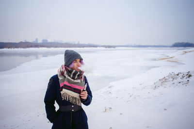 Young woman using phone while standing on snow covered beach