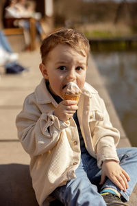 Little adorable boy sitting outdoors and eating ice cream. lake, water and sunny weather.