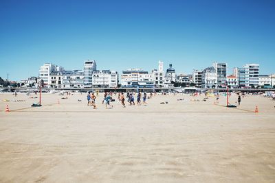 People on beach by buildings against clear sky