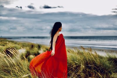 Rear view of woman standing at beach against sky