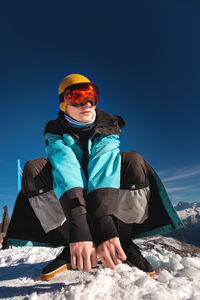 Man sitting on top of a hill. young man squatting in warm clothes on a sunny day in the snowy