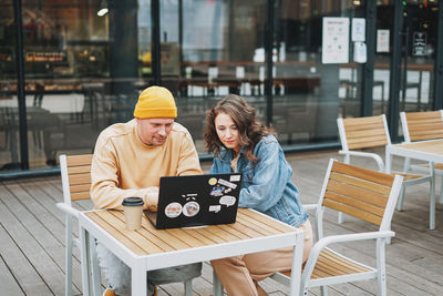 Stylish young couple freelancers working on laptop in street cafe