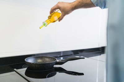 Man cooking in the kitchen in a denim shirt. an anonymous man is pouring olive oil into the pan