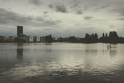 Scenic view of river by cityscape against sky