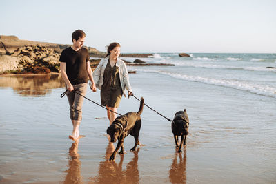 Couple with two dogs holding hands while walking at beach with dogs