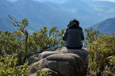 Rear view of woman sitting on rock against mountains