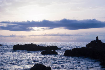 Silhouette rocks on sea against sky during sunset