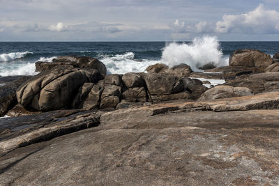 Waves splashing on rocks at shore against sky