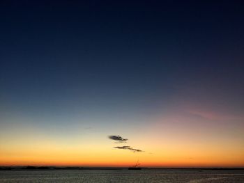 Couples sitting on bench by silhouette palm trees against sky during sunset