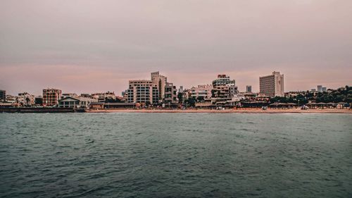 Sea by buildings against sky at dusk