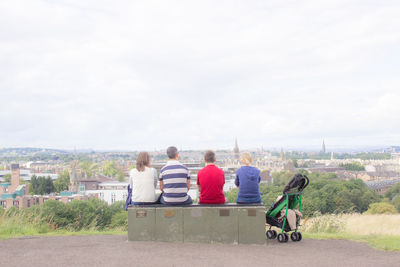 Rear view of family sitting on bench against sky