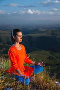 Young yogi woman practicing meditation with closed eyes in lotus position at sunset