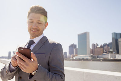 Portrait of a young businessman using his smartphone on a rooftop overlooking the city