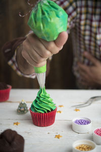 Midsection of man icing on cupcake at table